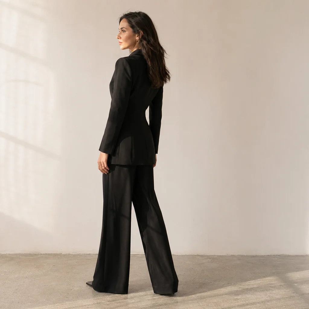 Fashion editorial portrait, natural window light. A woman standing in profile, her body turned sligh